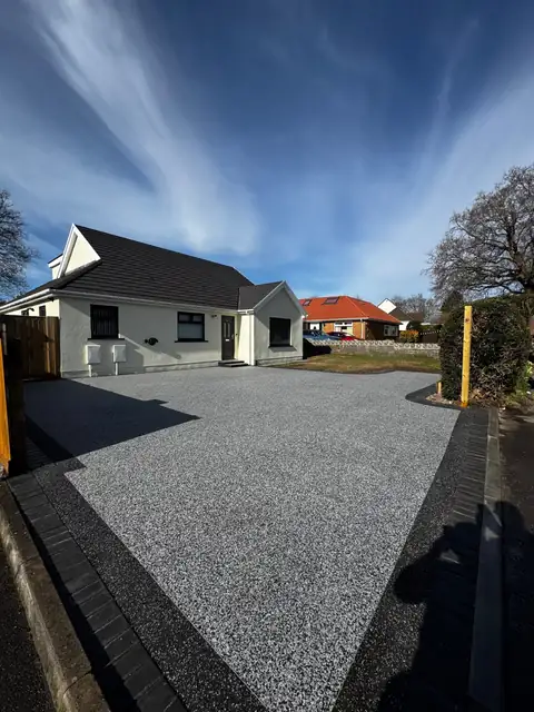 A wide grey resin driveway running the full frontage of a white rendered bungalow