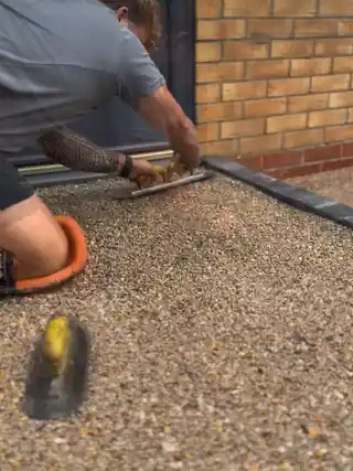 An installer trowelling resin bound stone tight against block edging